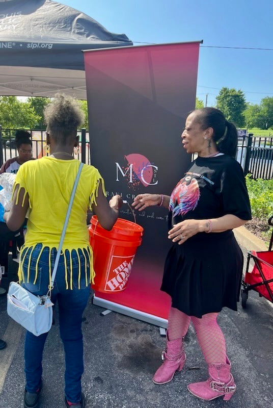 Founder hands disaster-relief bucket to resident at outdoor recovery event in St. Louis.
